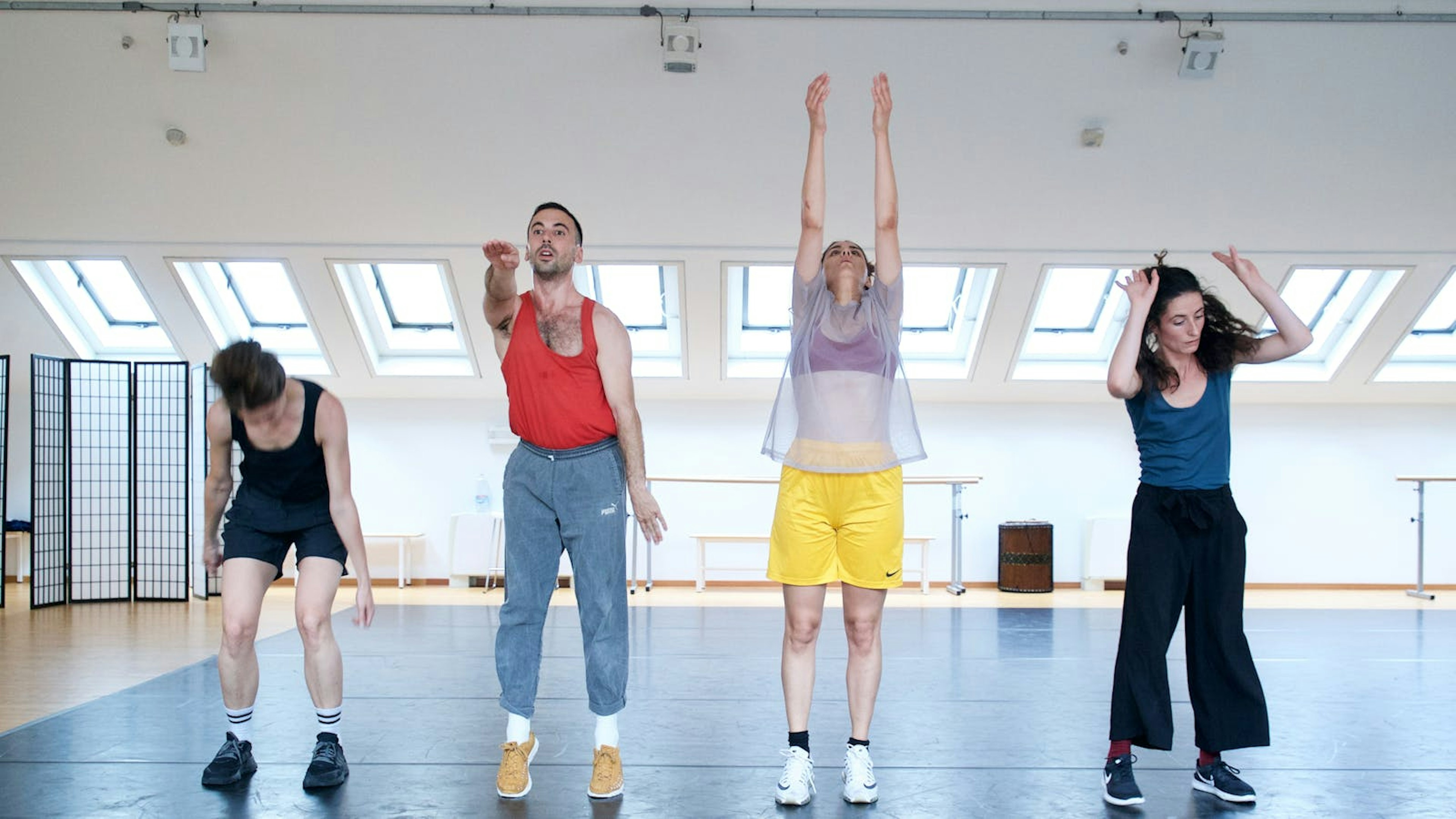 Quattro performer in fila orizzontale nello Studio fanno diversi movimenti con le braccia
