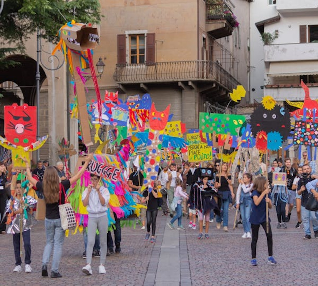 Una parata di giovanissimi nelle strade di Rovereto. Hanno cartelli molto colarati realizzati con l'artista e marciano per l'attenzine all'ambiente