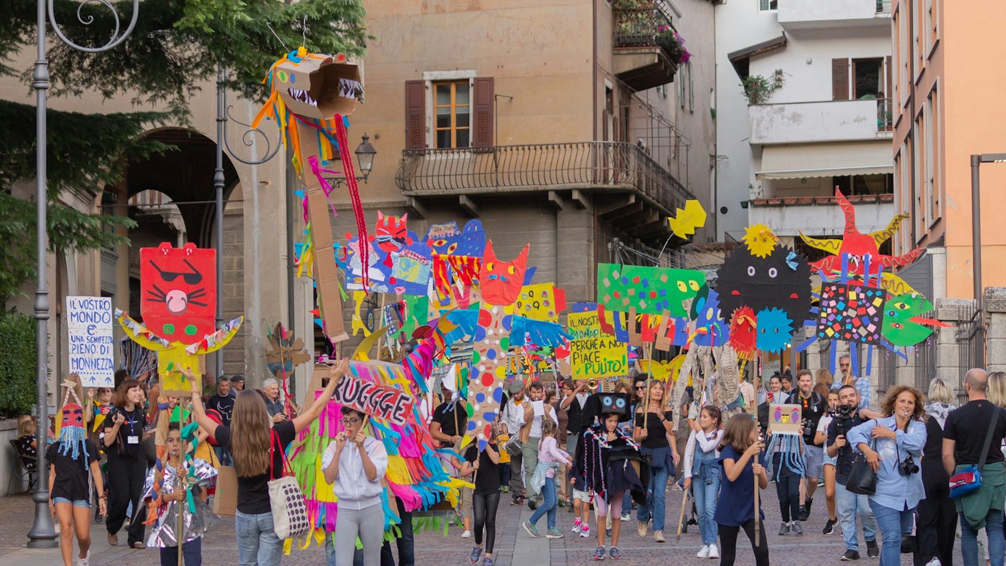 Una parata di giovanissimi nelle strade di Rovereto. Hanno cartelli molto colarati realizzati con l'artista e marciano per l'attenzine all'ambiente